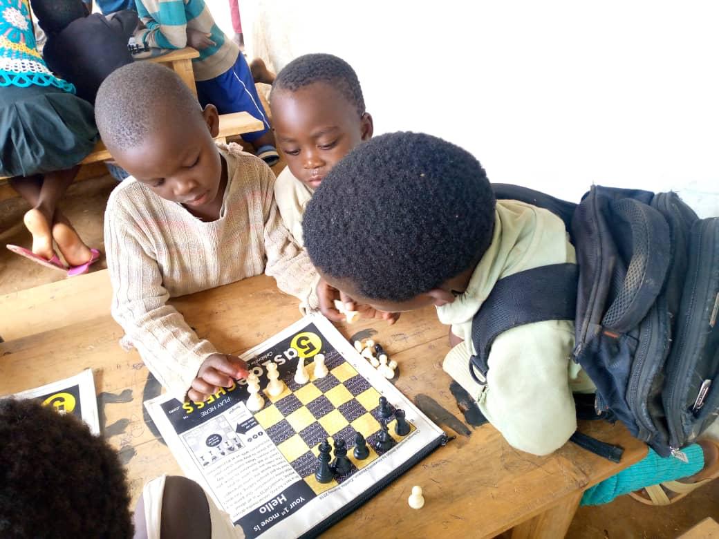 Three children playing on a roll-up 5asideCHESS board in a classroom in Uganda
