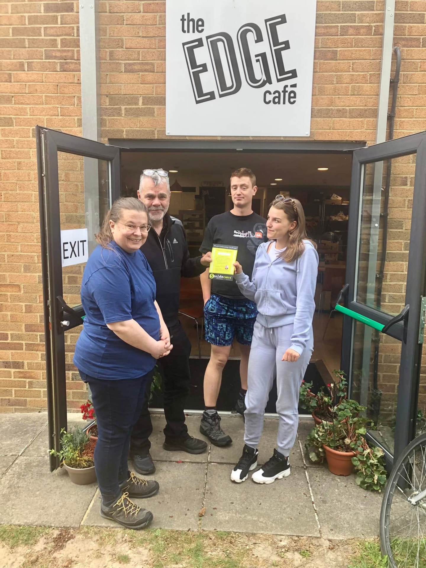 April with three others outside the Edge Café, holding her 5asideCHESS World Citizenship Challenge certificate