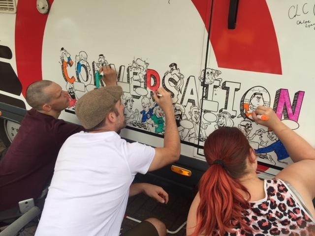 People signing the word CONVERSATION on the side of the Battling Suicide Bus at Braintree Foyer